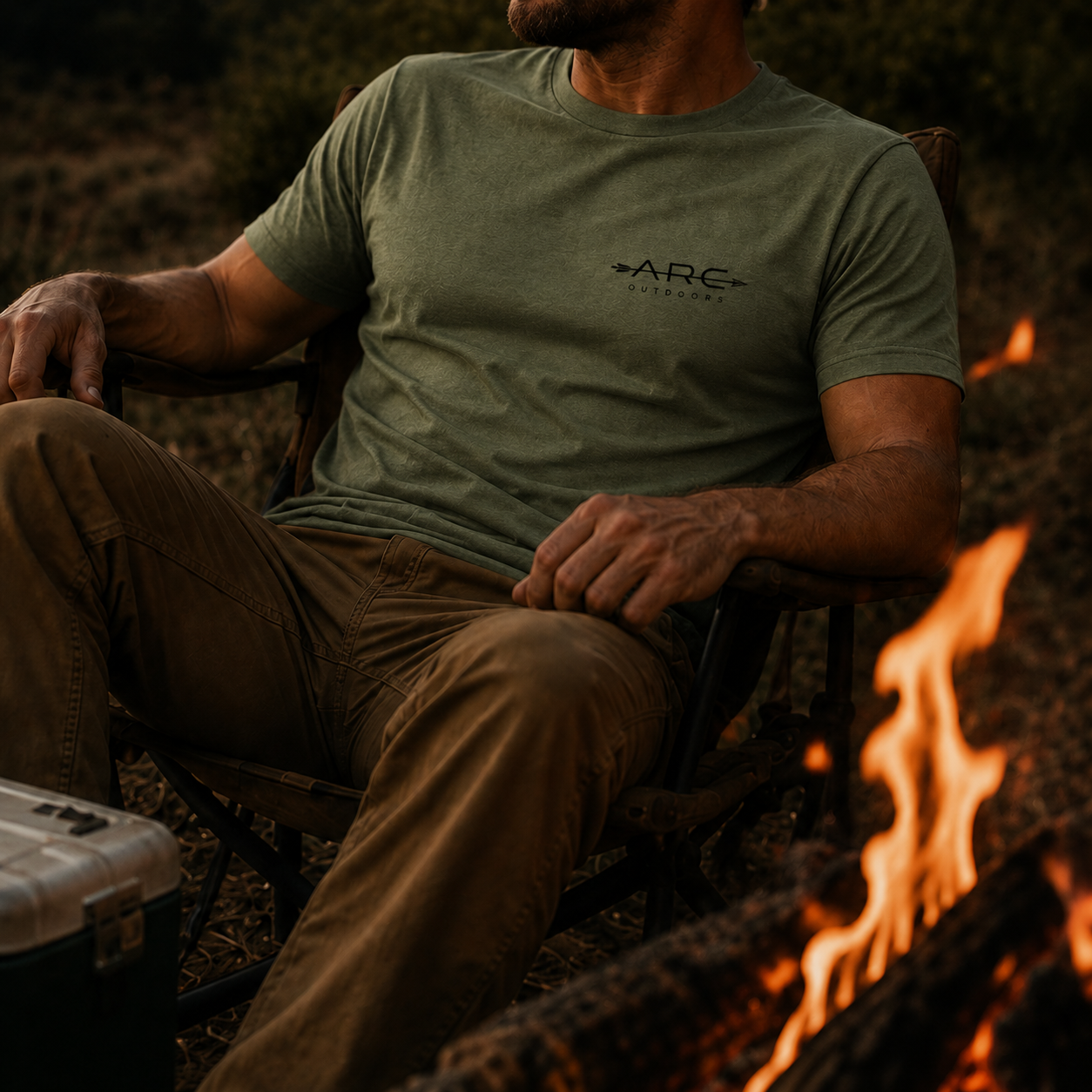 Man wearing field olive ARC Outdoors tee by a campfire