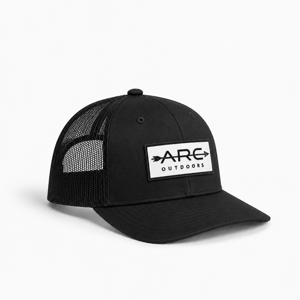 A black trucker-style cap with a white rectangular patch on the front that reads 'ARC OUTDOORS' with arrow graphics, shown on a clean white background.