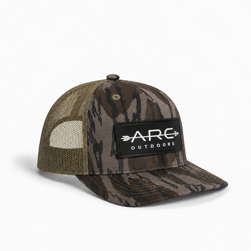 A camouflage trucker hat with olive green mesh back panels and a black front patch featuring the white 'ARC OUTDOORS' logo, shown on a clean white background.